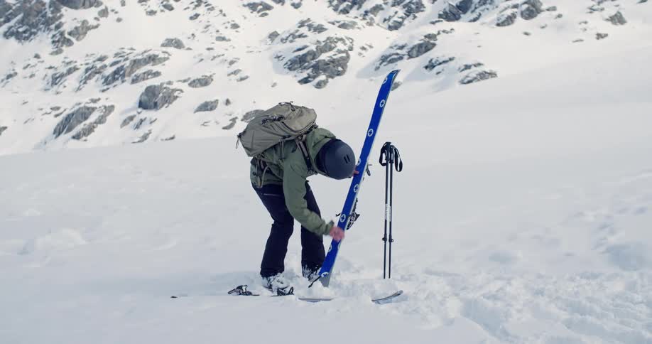 Man attaches covering to ski while standing on snow at base of mountain