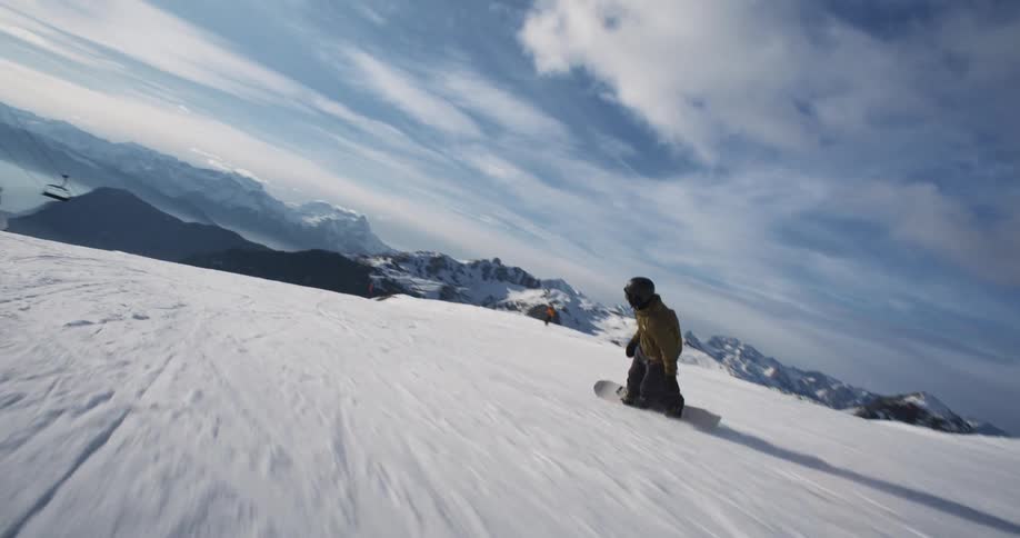 Following a snowboarder sliding on the white snow on the slopes of a mountain at morning