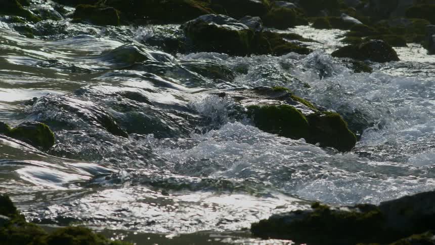 The current flows around stones in a river during the day