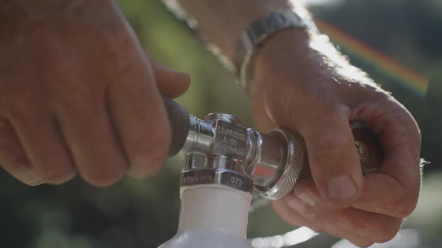 A person carefully twists a knob on a gas cylinder while outside