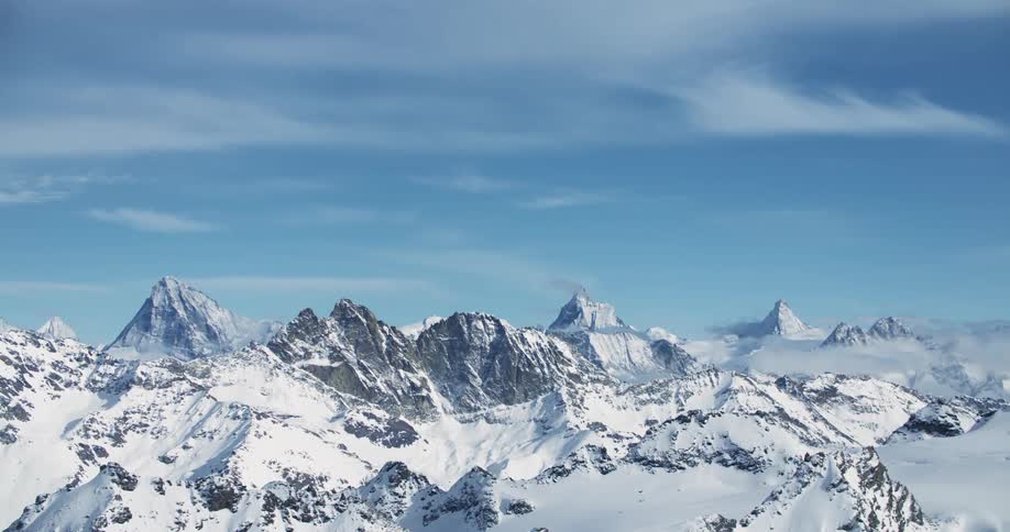 Snow capped mountain range under blue skies and white clouds