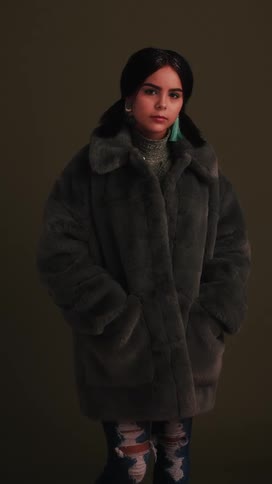 Woman with long black hair stands with her hands in her coat pocket