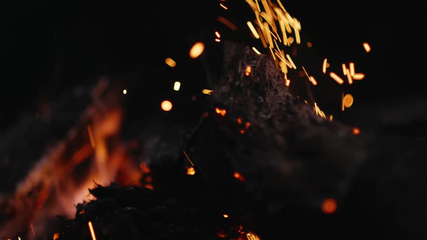 Flames and embers glow in the darkness as they rise from burning wood