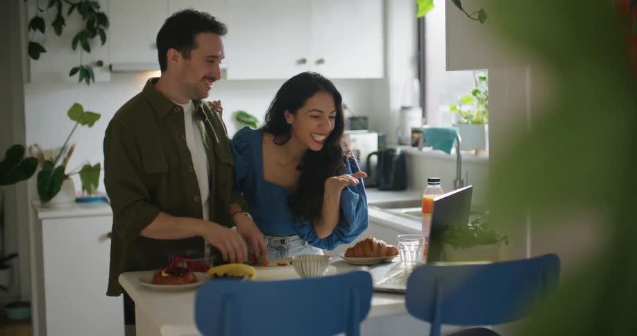 A man and woman smile as they talk to someone else via a video call on their laptop
