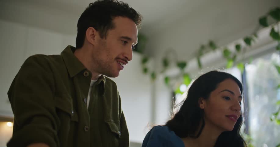 A man and woman chat while using a laptop together in the kitchen