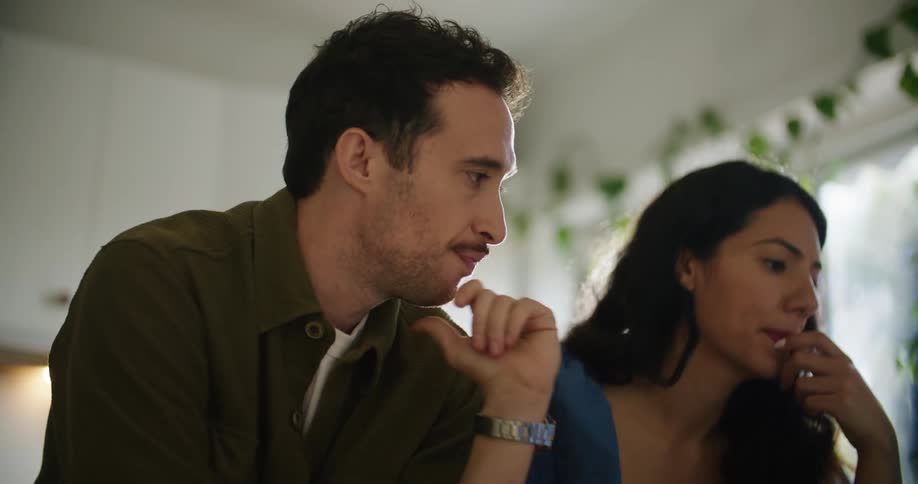 A man and woman sit at a breakfast bar in a kitchen with plates of food and discuss something they are looking at