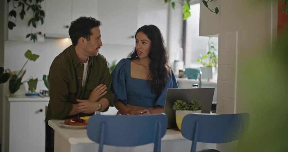 Young couple have a conversation in the kitchen at home while browsing on a laptop