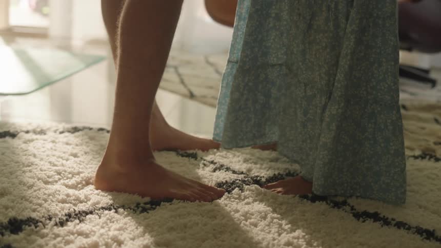 Close up of the bare feet of two woman standing in front of each other over a rug in the living room