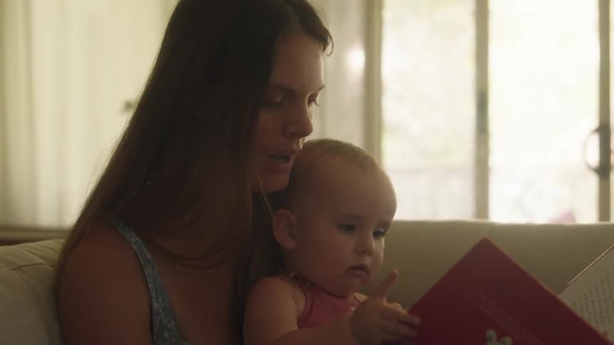 Close up of a mother reading a story book to her baby daughter at home