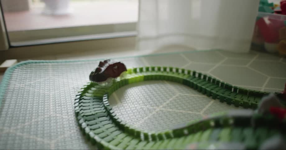 Car running on tracks of plastic toy train set in playroom on the floor with child in the background