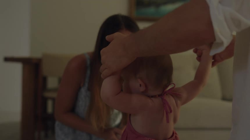 Parents teaching her daughter to walk in the living room at home