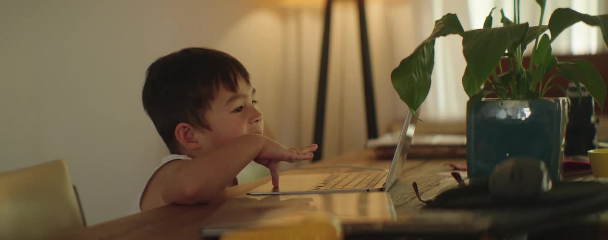 A little boy is sitting at a table playing on a laptop computer