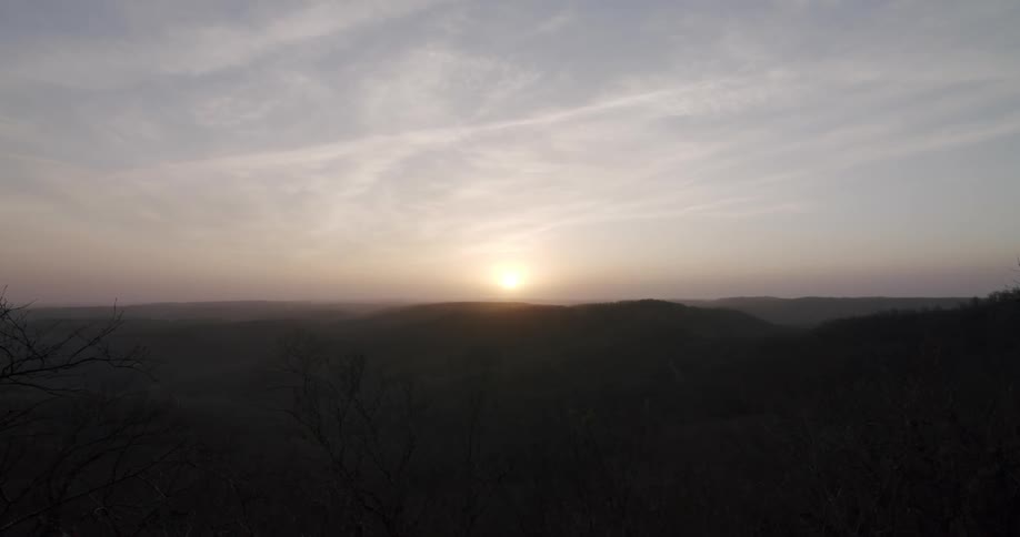 The sun is setting over mountains in a milky white cloudy sky
