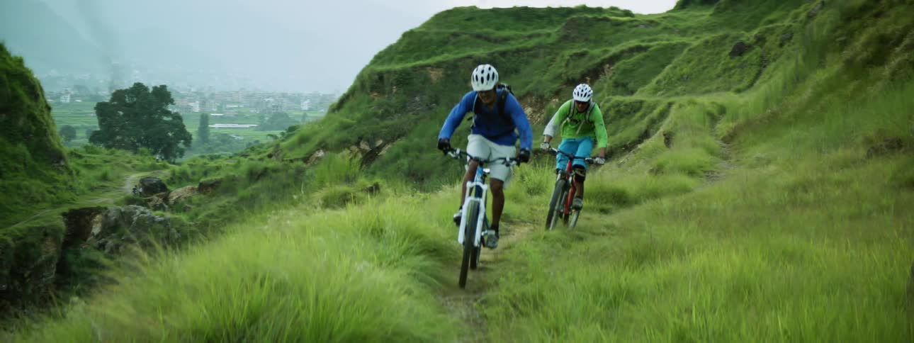 Two men mountain biking through grassy canyon during the day
