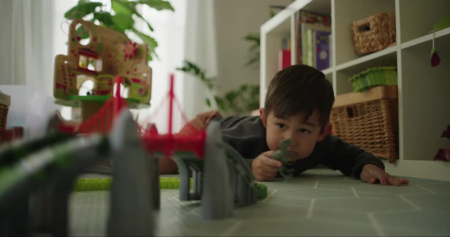 A little boy lays on the floor watching a toy racecar go around a toy racetrack
