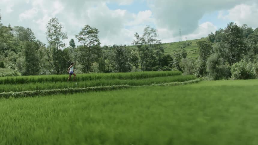 Determined woman with white shirt and purple shorts runs in the green field