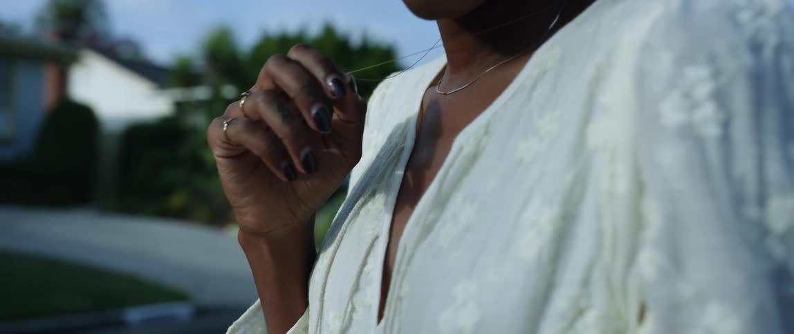 Woman standing outside of house in residential neighborhood grasping charm on necklace pondering something