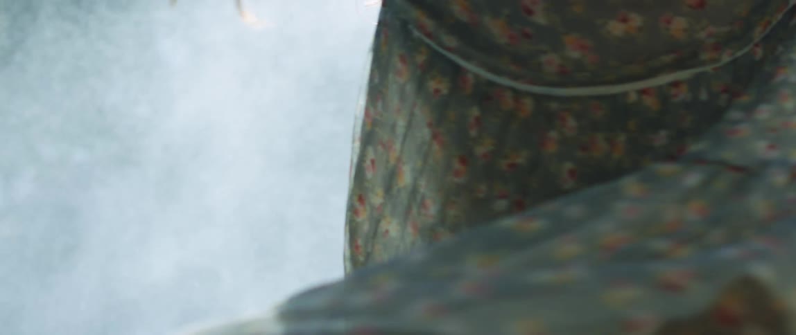 A woman in a sheer dress spins around while surrounded by smoke