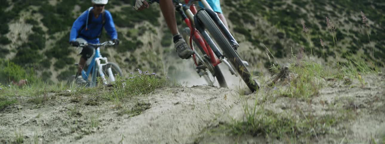 Two people riding their bikes through a mountain trail wearing helmets