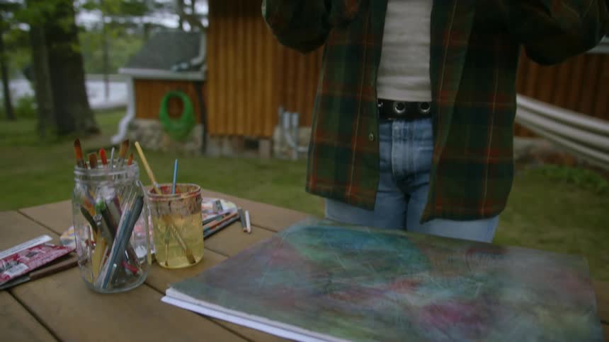 Standing outside house near water female artist takes picture of painted canvaswith a smartphone