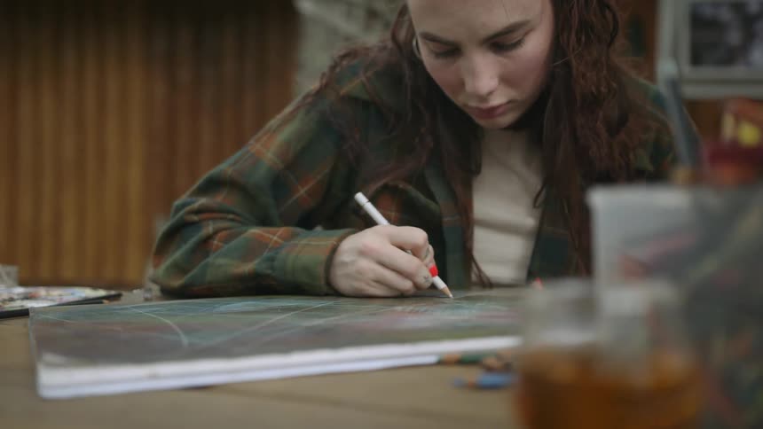 A young woman sits outdoors while working on a large drawing