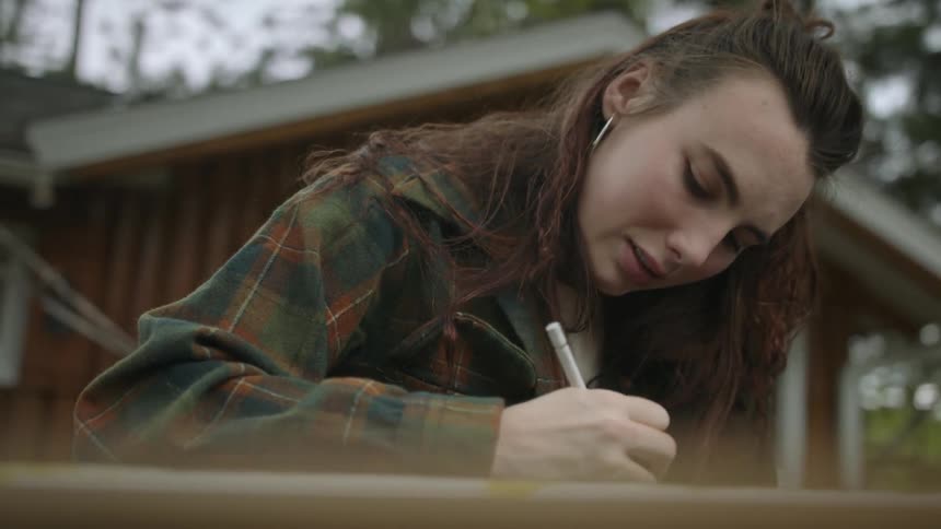 A woman sitting outside drawing with a white pencil