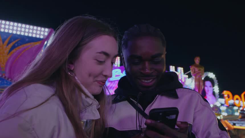 A man and woman look at a phone together while at a carnival