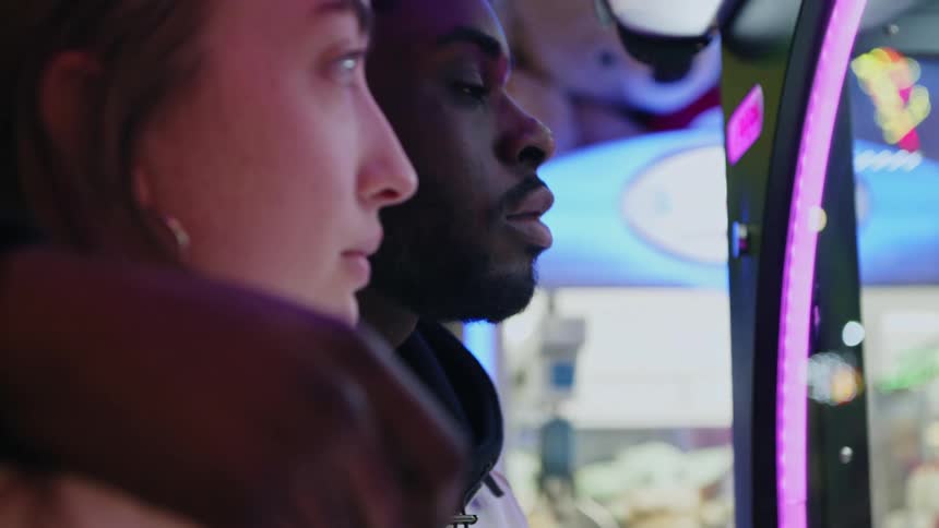 A young man and woman watch attentively as they play a carnival game together