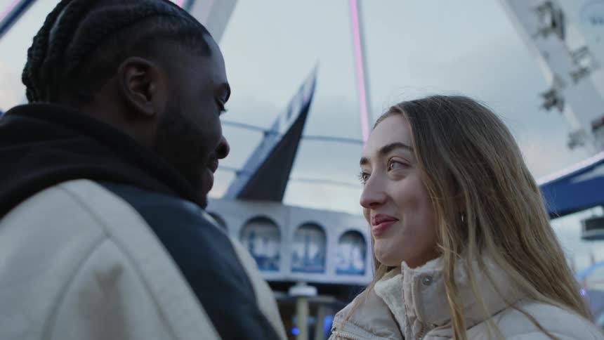 A man and woman stand close together while chatting outside a carnival ride
