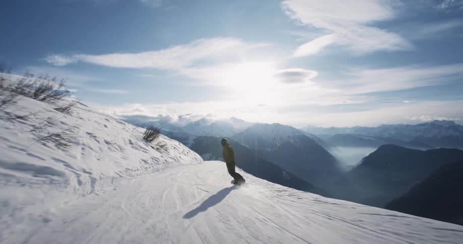 A snowboarded races down a steep mountain road under partly sunny skies