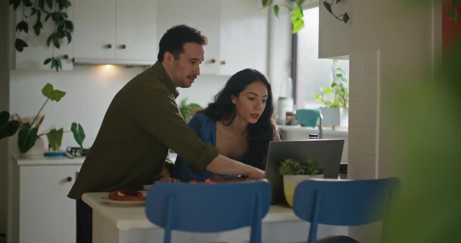 Man and woman standing at breakfast counter in kitchen looking at laptop and discussing home decor options