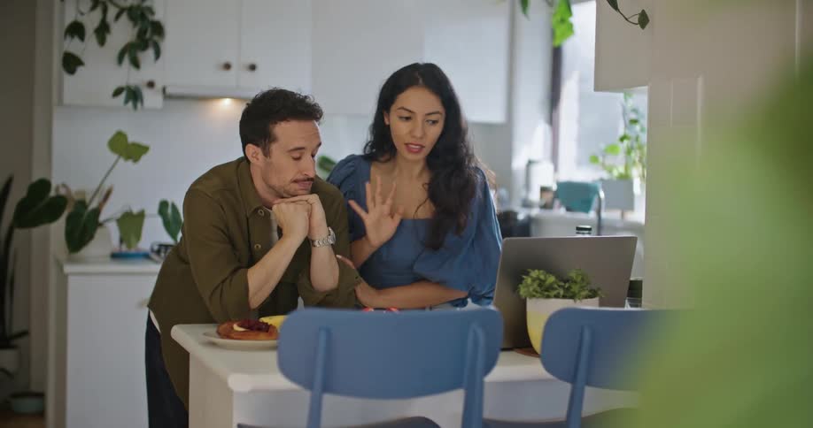 Man and woman stand at table with laptop and food and hold a conversation