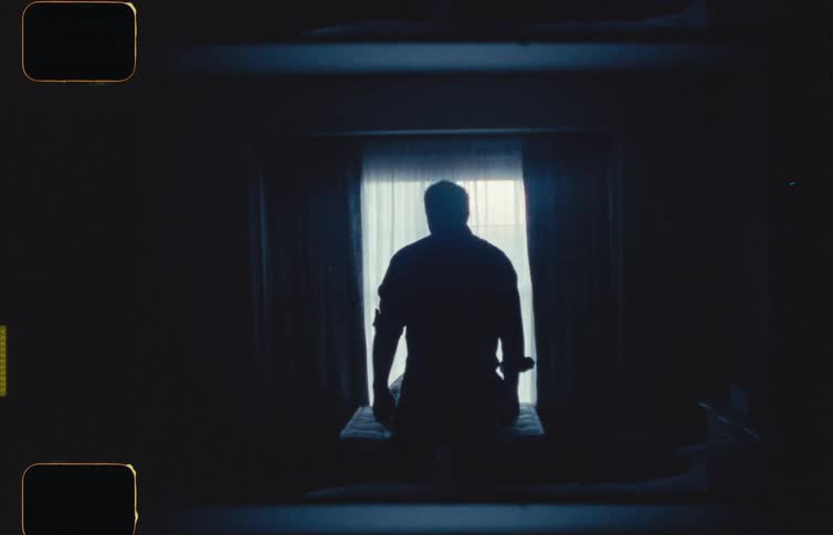 The silhouette of a man standing in front of a window with light shining through the curtains as the man walks away