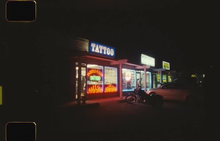 A parking lot outside of a tattoo parlor at night