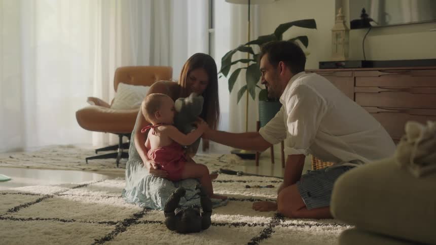 A mother and father smile while playing with their infant daughter