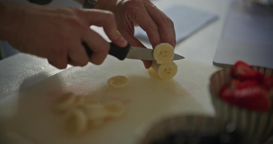 A man slices up a banana next to bowls of fruit