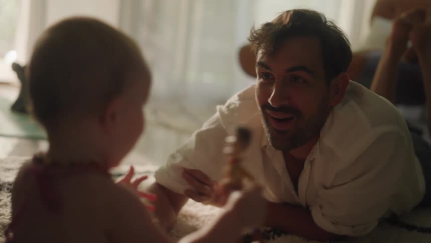 Father with stubble beard and white shirt plays with toddler daughter in the living room