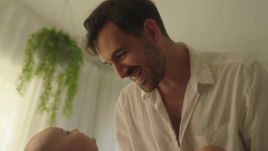 A man smiles and talks looking down at the baby in his arms