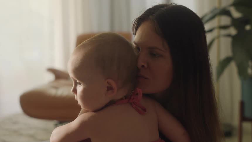 A mother holding her baby daughter and kissing her on the head with they sit on the floor