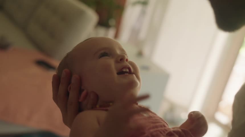 A father holding his baby daughter in his arms and hands while he bounces up and down and smiles and laughs at the baby