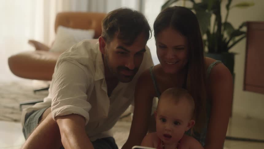A father mother and baby sitting on the living room floor posing for a picture on the mans cell phone