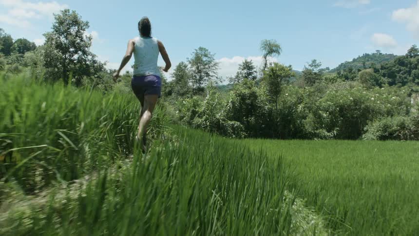Woman Running Along Narrow Dirt Path Through Tall Grass