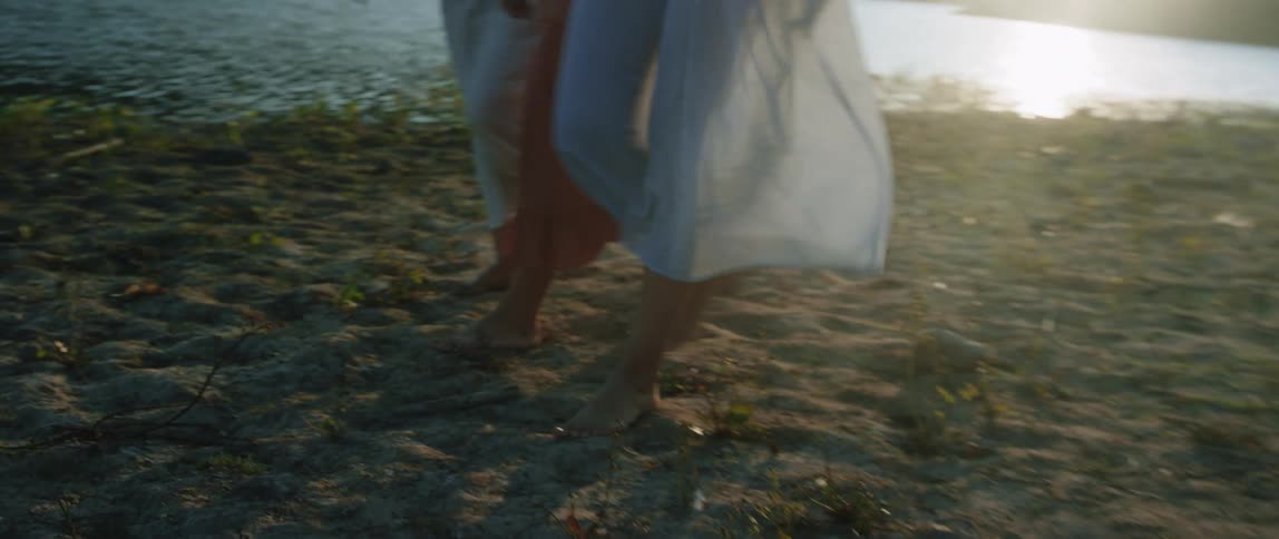 Women walking on the beach together wearing dresses near the water