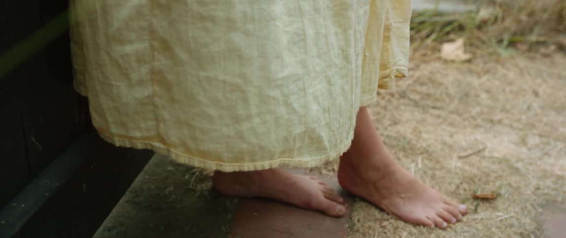 Woman wearing yellow dress stands barefoot near gate