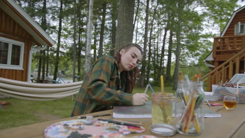 A woman sitting outside at a table while she draws on a canvase