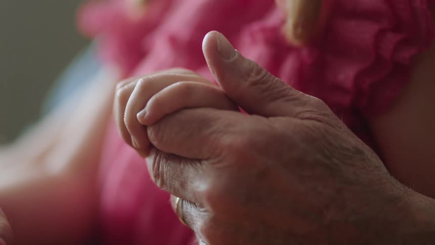 An up close of an older persons hand holding a childs hand and rubbing their thumb over it
