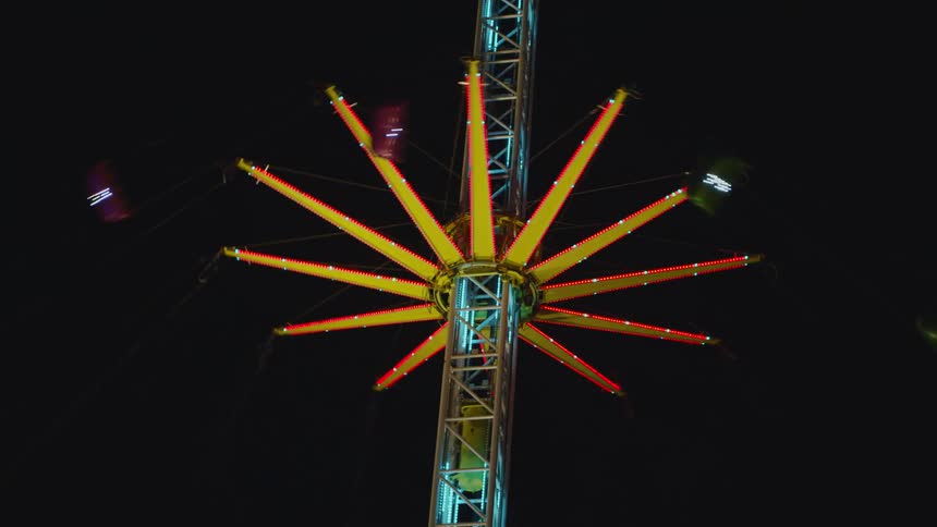 An amusement park swing ride lit up in neon twirls riders around at night