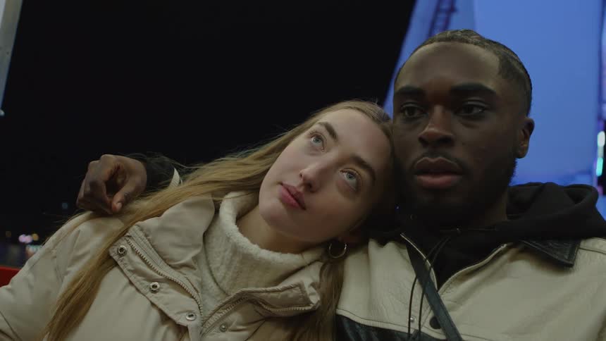 Young woman and man enjoying a romantic ferris wheel ride together at nighttime at the amusement park