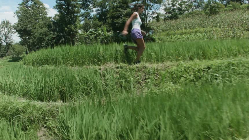 A woman running on a path next to tall fields of grass