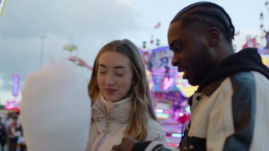 A man and woman share cotton candy while at the fairgrounds